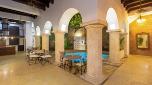 A poolside area with stone columns, a pool, and a seating arrangement. - Hotel Boutique Patio Corao By GEH Suites (Cartagena)