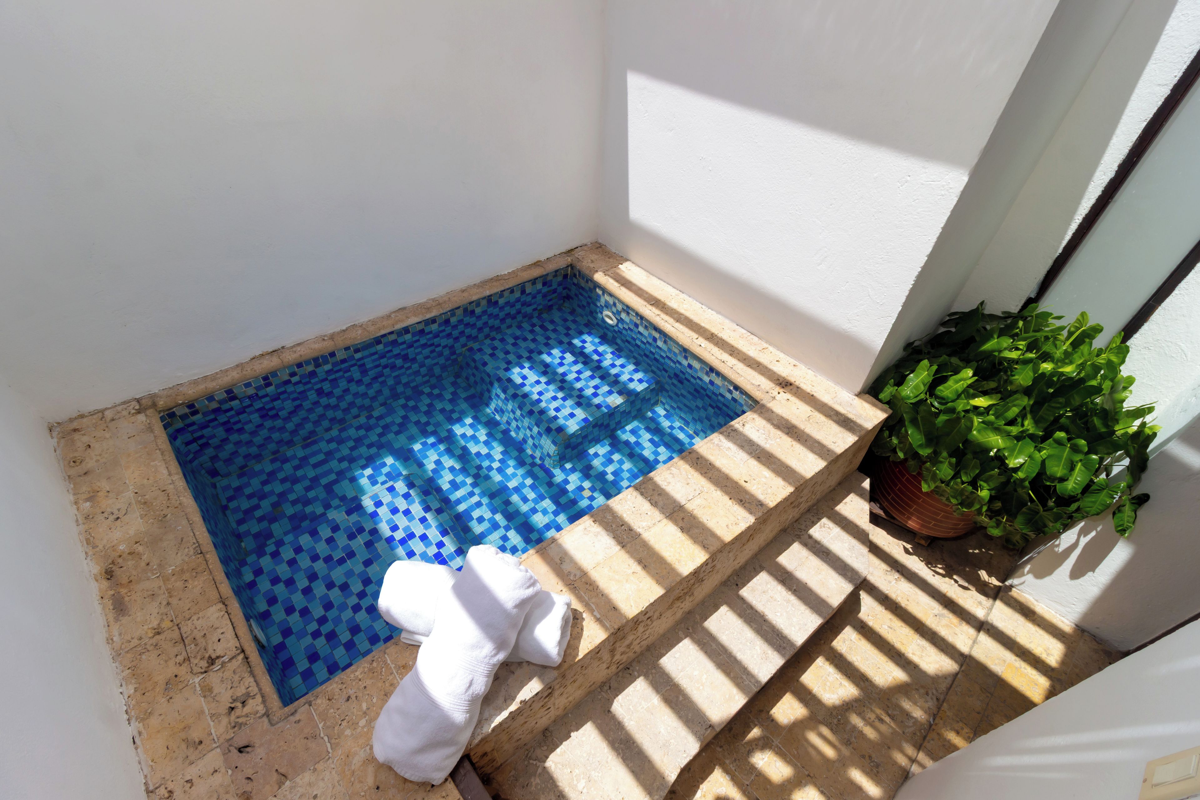 A small pool with blue mosaic tiles, a white towel, and a potted plant.