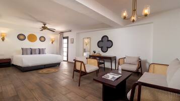 A hotel room with a bed, two chairs, a coffee table, a desk, a ceiling fan, wall sconces, and a chandelier.