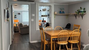 Un comedor con una mesa y sillas de madera, una cocina al fondo y un pasillo que lleva a otra habitación.