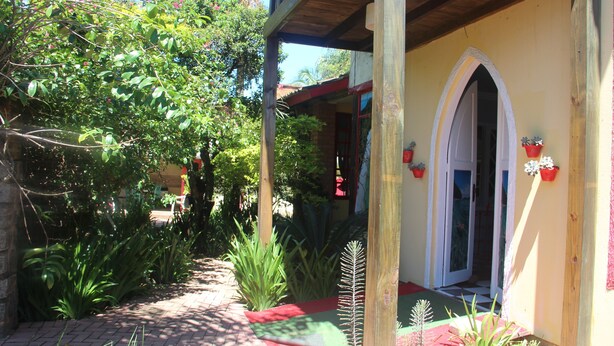 A covered outdoor area with a wooden structure, a red and green pathway, and various potted plants. - Pousada To na Praia Campeche (Florianopolis)