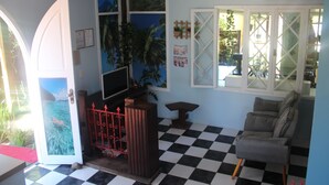 A room with a checkered floor, a grey sofa, a TV, a red gate, and a door with a tropical mural. - Pousada To na Praia Campeche (Florianopolis)