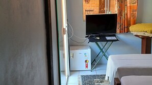 A hotel room with a bed, a TV, a small table, a heater, and a window with curtains. - Pousada To na Praia Campeche (Florianopolis)