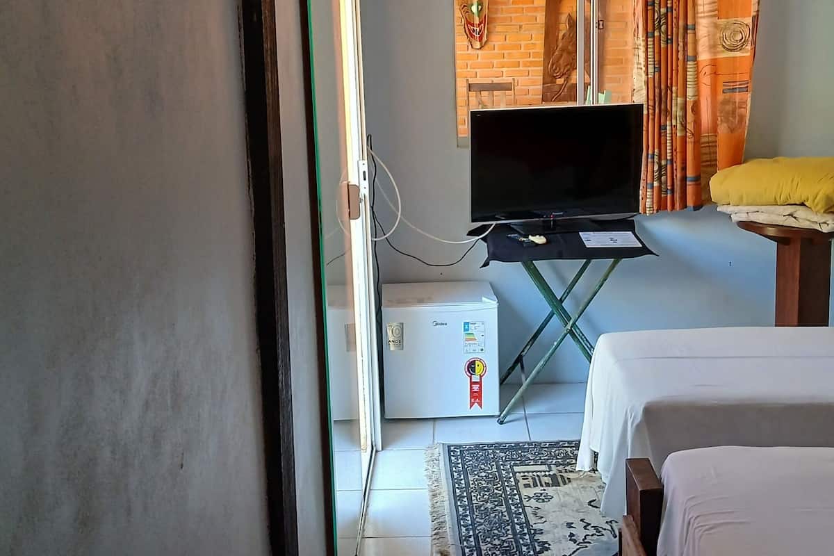 Quarto de hotel com cama, televisão, uma pequena mesa, aquecedor e janela com cortinas.