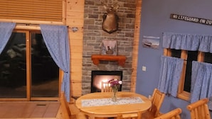 A wooden interior with a round table and chairs, a fireplace, and a stone wall.