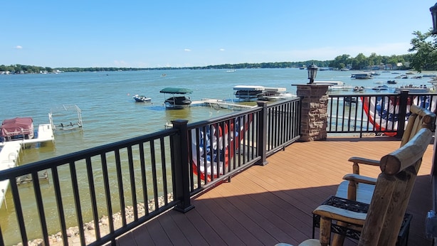 A wooden deck with a railing overlooking a lake with boats.