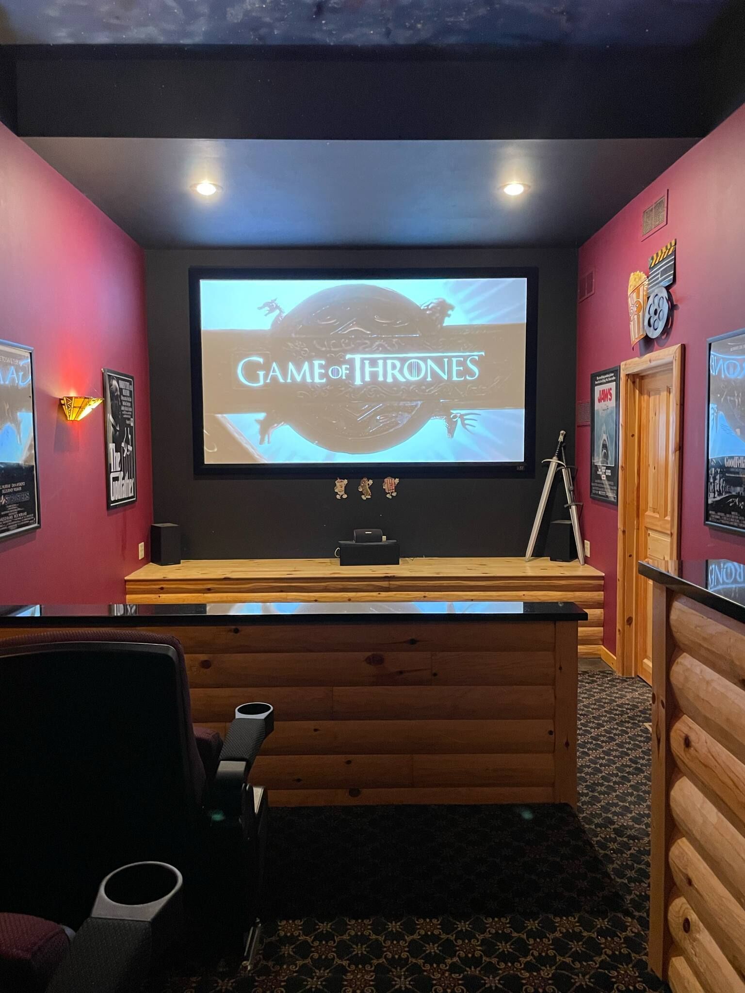 Una habitación acogedora con una pantalla grande mostrando 'Game of Thrones', paneles de madera y un proyector.