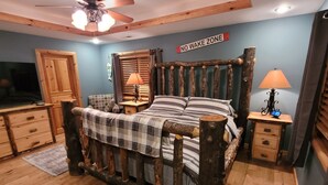A bedroom with a rustic bed, wooden floors, a ceiling fan, and a 'No Wake Zone' sign.