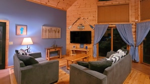 A cozy wooden cabin interior with two sofas, a TV, and a fireplace.