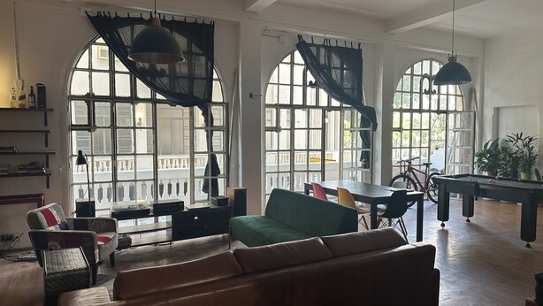 A spacious living room with a green sofa, a dining table, and a pool table. Large windows with curtains provide natural light and views of the outside. - A unique loft in the historic center of Rio de Janeiro. (Centro Rio de Janeiro)