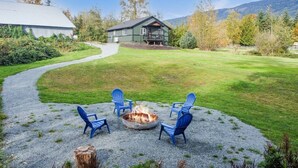 Eine gepflegte Schottersitzterrasse mit einem Feuerkorb und vier Adirondack-Stühlen, ein Haus mit begrüntem Dach und ein Weg dorthin.