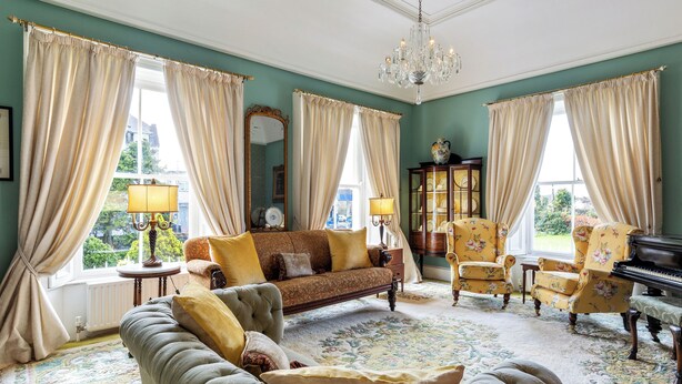 Uma sala de estar ampla com sofá, poltronas, um piano e um espelho grande.