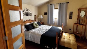 Un dormitorio con una cama, un banco de madera, una mesita de noche, una lámpara y un espejo.