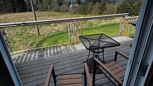 Una terraza con dos sillas de madera y una mesa de metal, con vistas a un campo cubierto de césped y árboles.