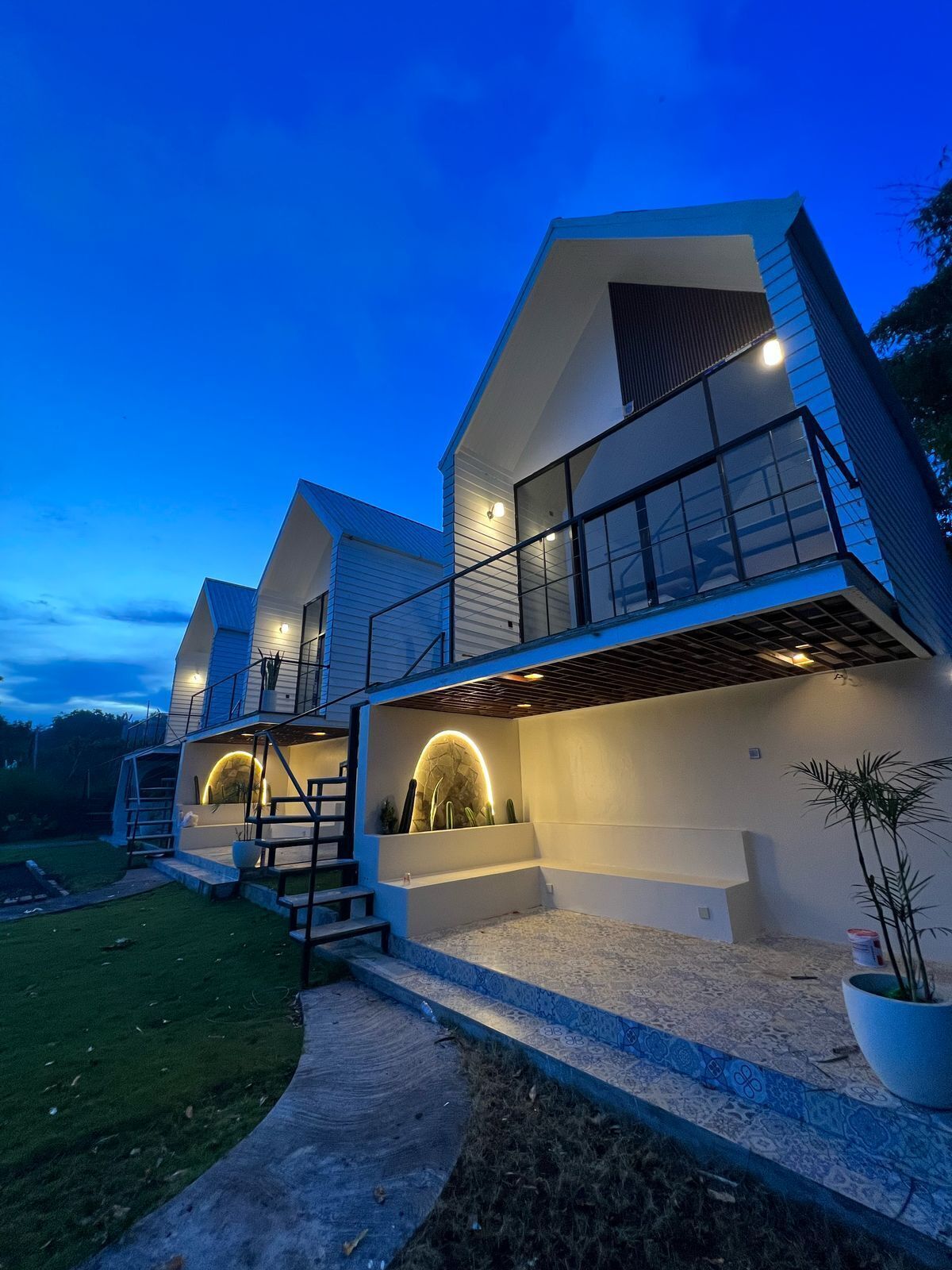 Una casa moderna de varios niveles, con un balcón destacado, un espacio exterior cubierto y una entrada bien iluminada.