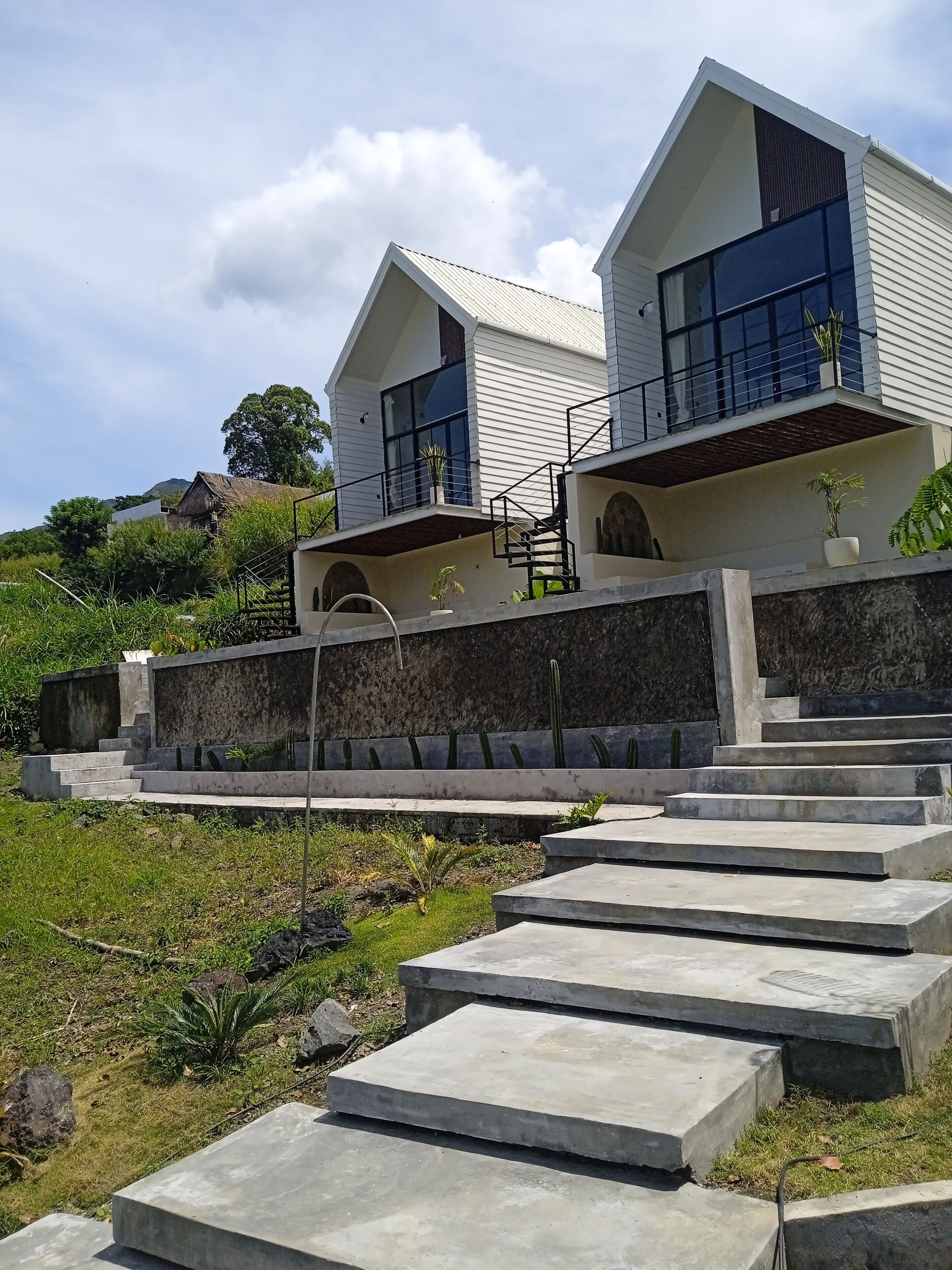 A modern two-story house with a stone retaining wall and concrete steps leading to a balcony.