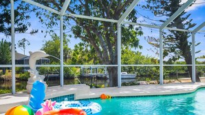 A pool area with a covered section, inflatable toys, and a dolphin statue. - Charming Paradise w/ Beautiful Pool and waterfront Tiki Hut + Backyard Boat Ramp (Port Charlotte)