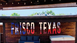 A covered outdoor seating area with a pool, a wooden wall with the text "FRISCO TEXAS" in large letters, and a blue sofa. - New House/with Pool/Hot Tub/Putting Green/Close to Universal Studios/Theme Rooms (Frisco)