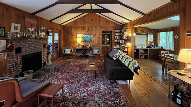 A rustic cabin interior with a fireplace, wooden walls, a sofa, a dining area, and a kitchen. - Grandparent’s Cottage 250 steps to the lake (Stockbridge)