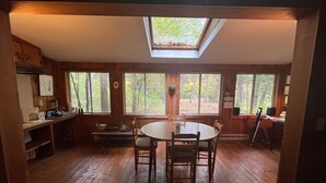 A wooden interior with a skylight, large windows, a dining table, and a kitchen area. - Grandparent’s Cottage 250 steps to the lake (Stockbridge)