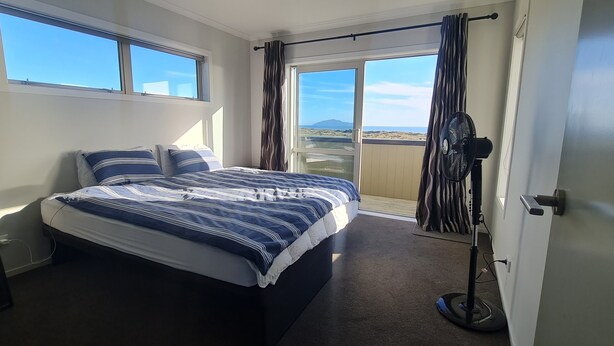 Un dormitorio con una cama grande, vistas a la playa por la ventana y un ventilador de techo.