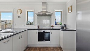 Una cocina moderna con armarios blancos, un lavamanos de acero inoxidable, horno empotrado y un amplio ventanal con vistas al exterior.