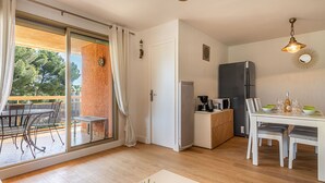 Eine moderne Küche mit Kühlschrank, Mikrowelle und Kaffeemaschine, ein Essbereich mit Tisch und Stühlen sowie eine Glastür, die auf eine Terrasse im Freien führt.