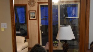 Una sala de estar con un sofá de cuero marrón, una puerta de vidrio que da a otra habitación, y una mesa con una lámpara.