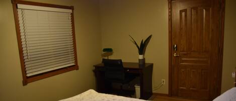 Un dormitorio con una cama, un escritorio, una silla, una planta en maceta y una puerta.