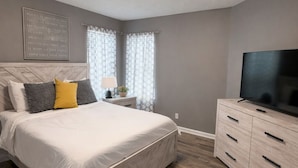 A bedroom with a bed, a nightstand, a dresser, and a television.