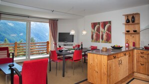 A modern kitchen with wooden cabinets, a dining area with red chairs, and a large window overlooking a mountainous landscape. - Les Combins 30 by Interhome (Champex)