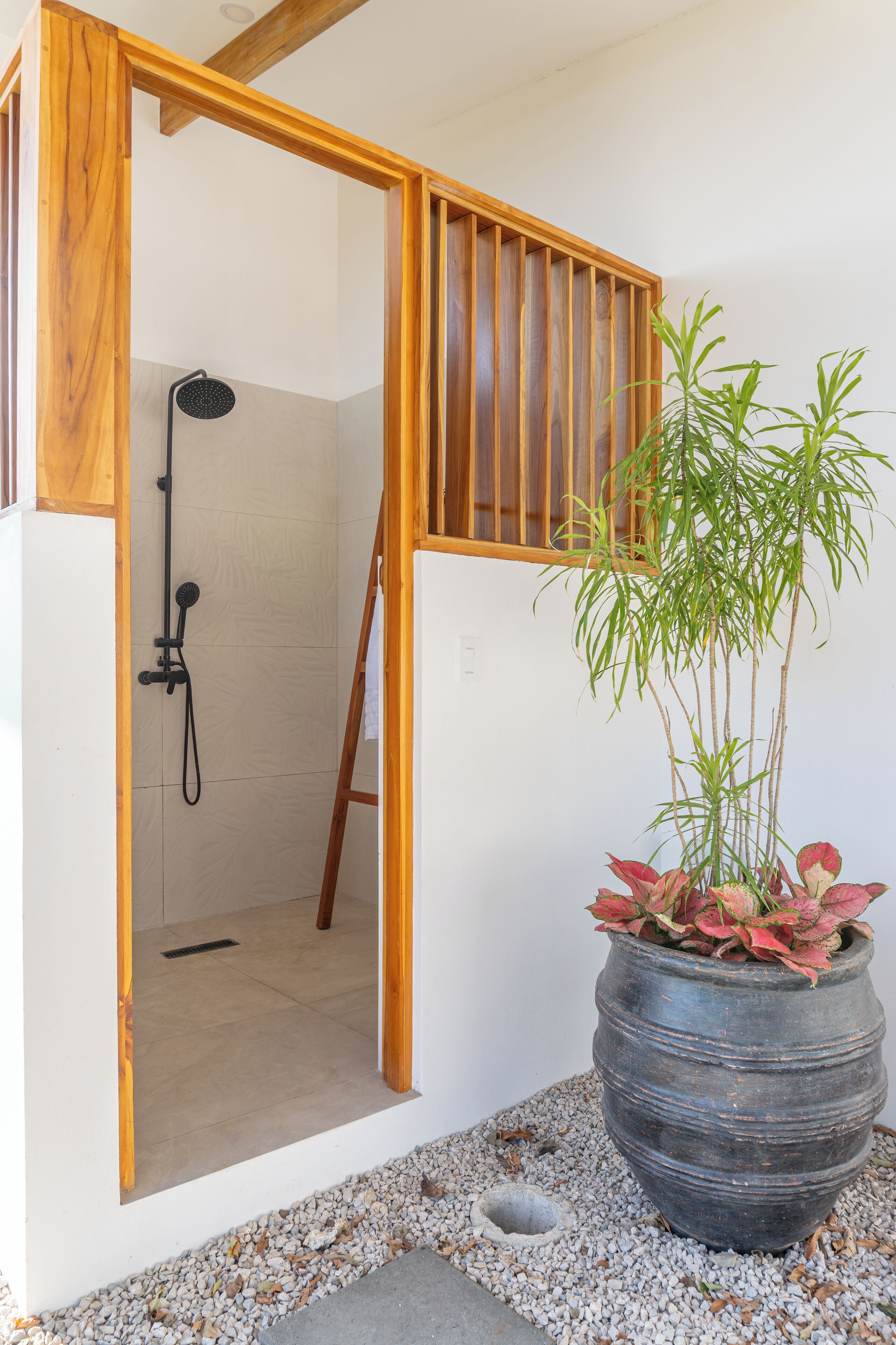 A wooden-framed shower area with a bamboo plant in a large pot.