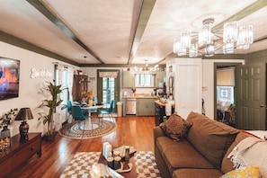 Uma sala de estar aconchegante com sofá, área de jantar com cadeiras, cozinha com armários e teto com lustre.