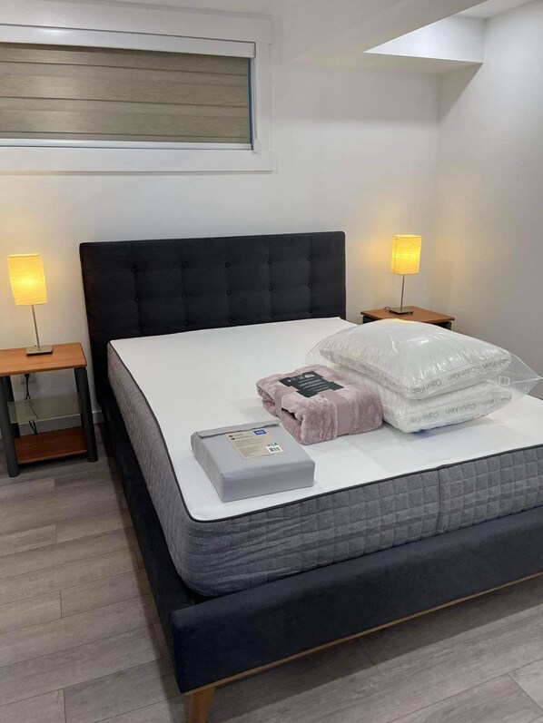 Une chambre moderne avec un grand lit, deux tables de chevet avec des lampes, une tête de lit en bois et une vue sur le ciel par une fenêtre.
