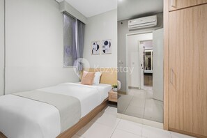 Une chambre à coucher comprenant un lit, une table de chevet, une fenêtre avec des rideaux, un climatiseur fixé au mur et une armoire en bois.