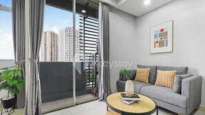Un salon moderne avec un canapé gris, une table basse ronde et une vue sur la ville grâce à de grandes fenêtres.