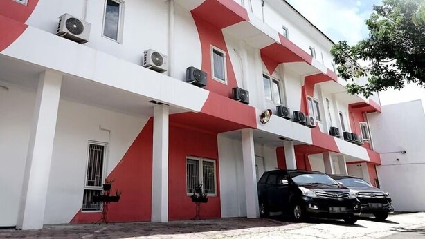 Un immeuble à plusieurs étages aux couleurs rouge et blanc, doté de balcons et de climatiseurs.