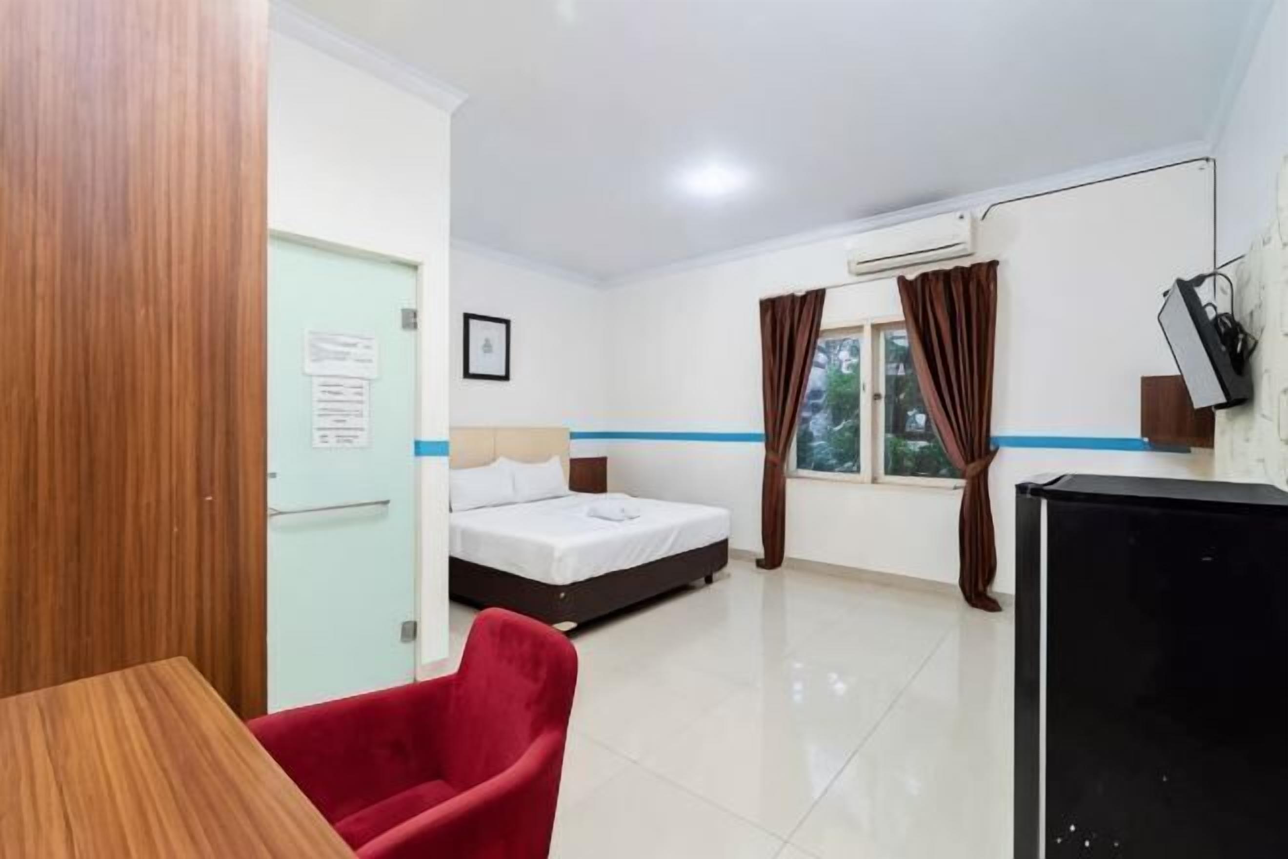 A hotel room with a bed, a desk, a chair, a TV, and a window with curtains.