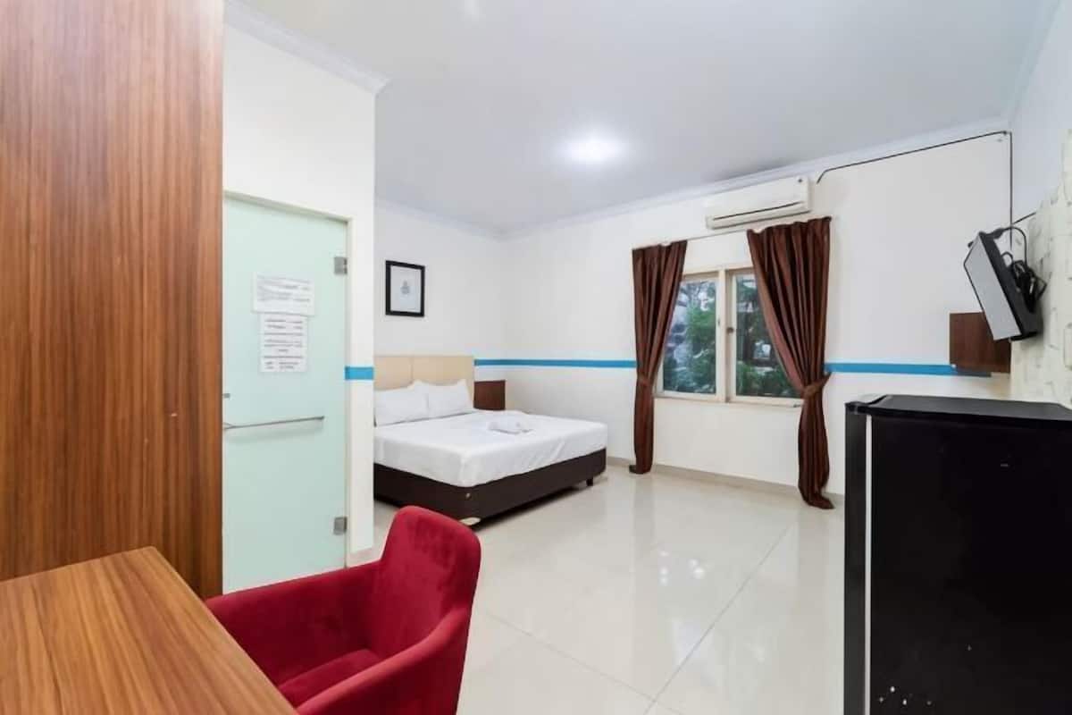 Une chambre d’hôtel avec un lit, un bureau, une chaise, une télévision et une fenêtre avec des rideaux.