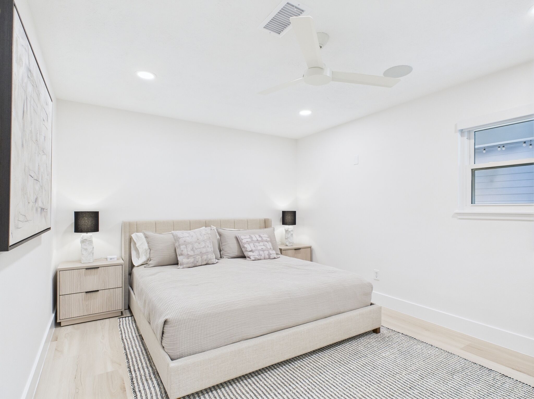 A bedroom with a bed, bedside tables, a ceiling fan, and a window.