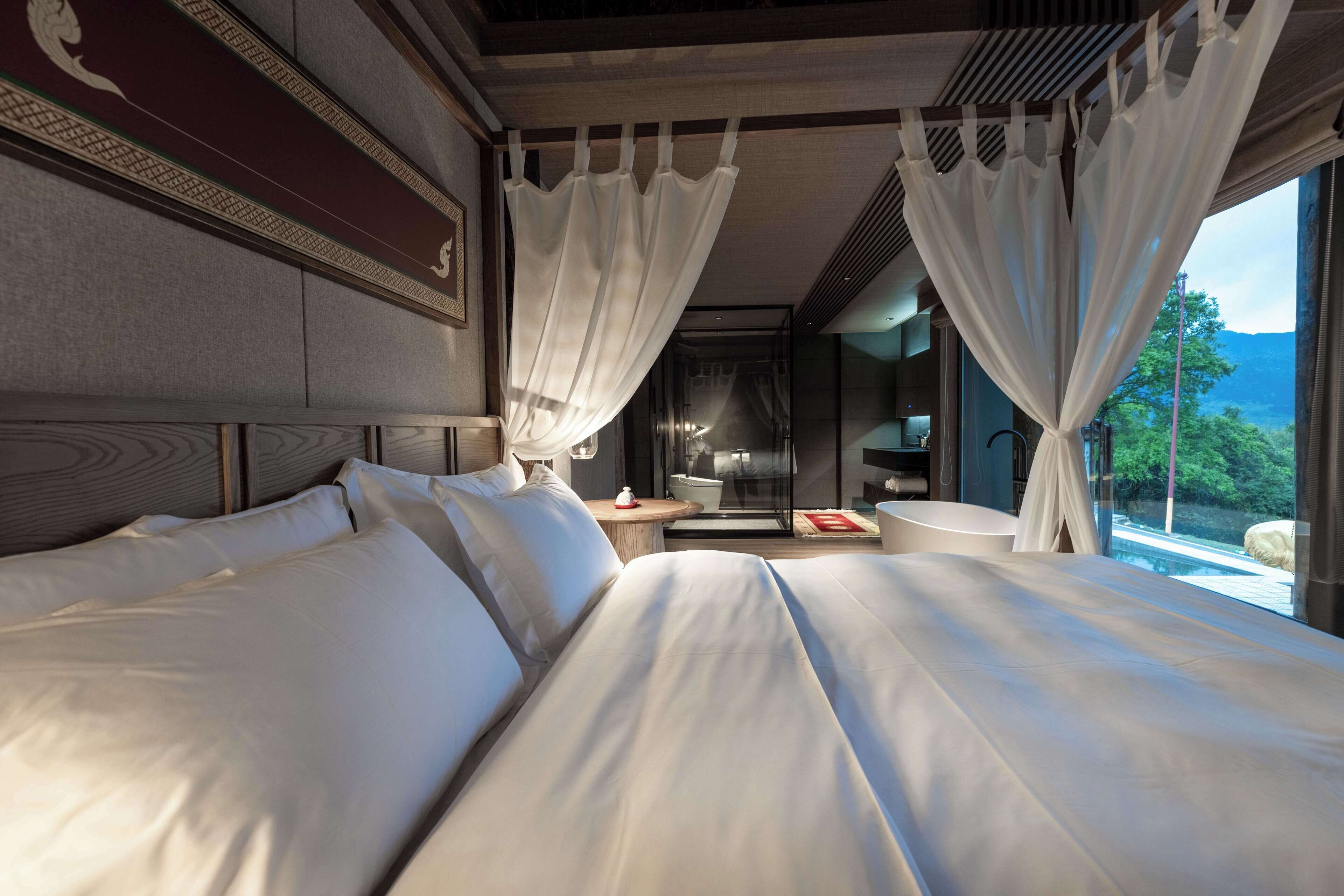 A modern hotel room with a large bed, a small round table, and a view of the outdoors.