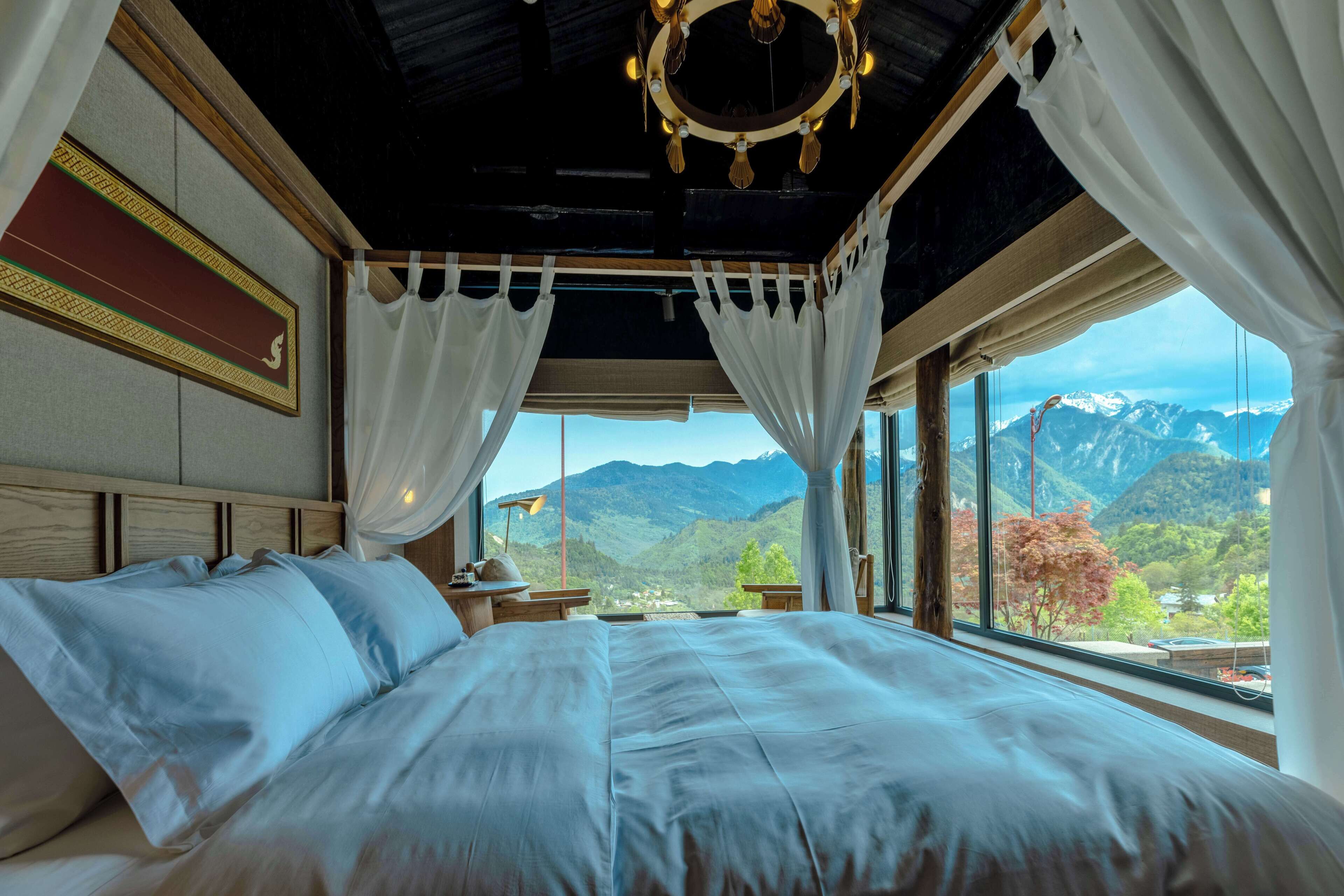 Una camera da letto con un letto grande, un lampadario e vista sulle montagne attraverso ampie finestre.