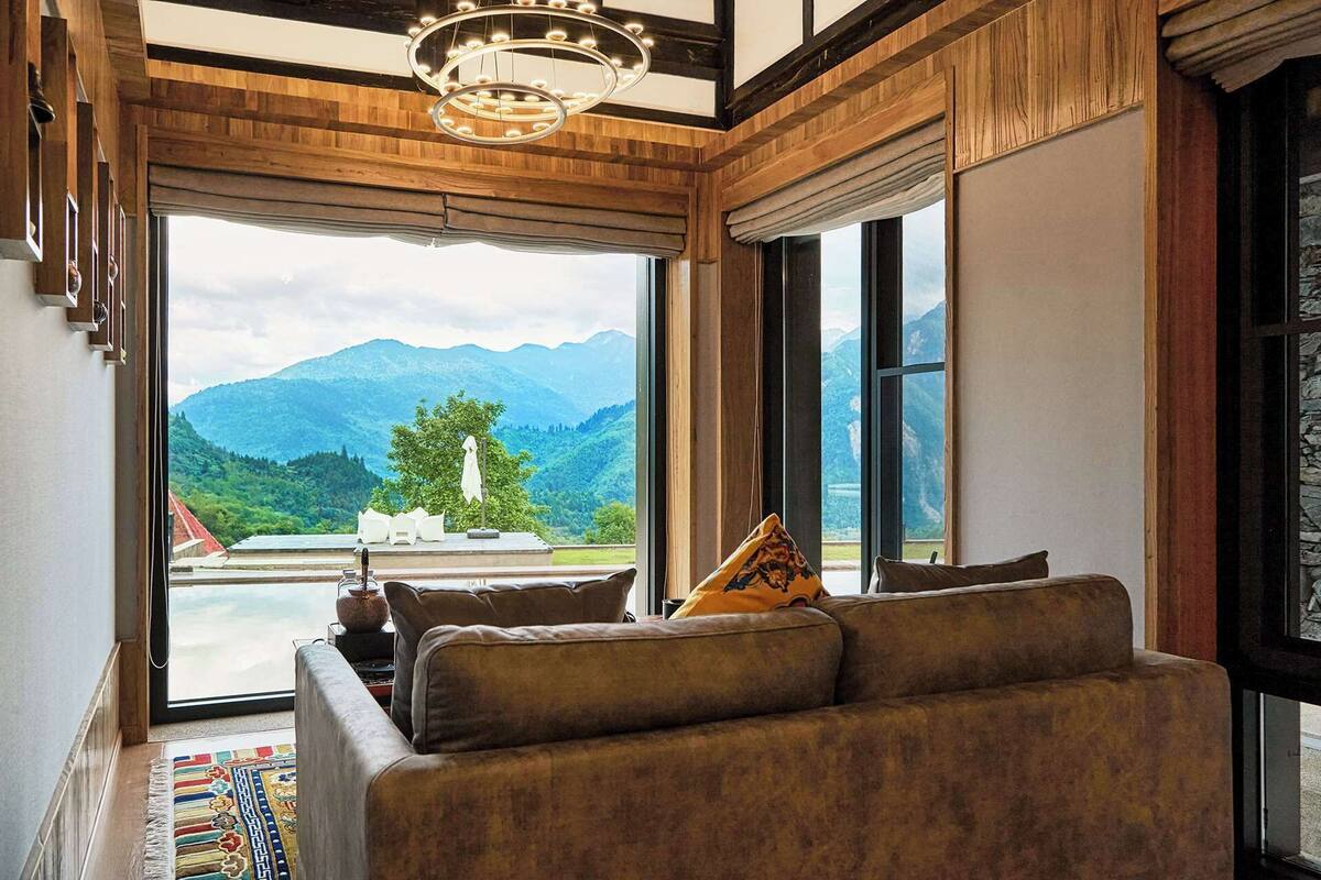 Ein Wohnzimmer mit einer Couch, einer Pendelleuchte und Blick auf Berge.