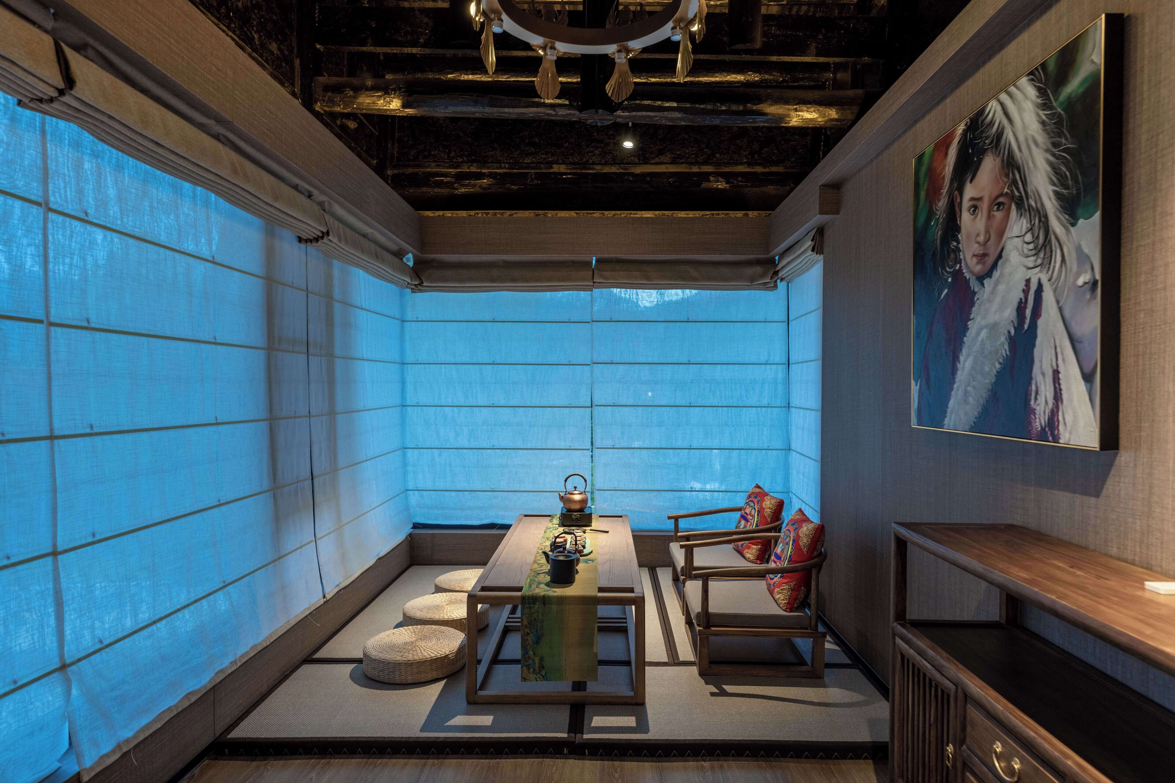 Ein Zimmer mit Tatami-Boden, einem niedrigen Tisch mit Tee-Service, einem Stuhl mit Kissen und einem großen Gemälde an der Wand.