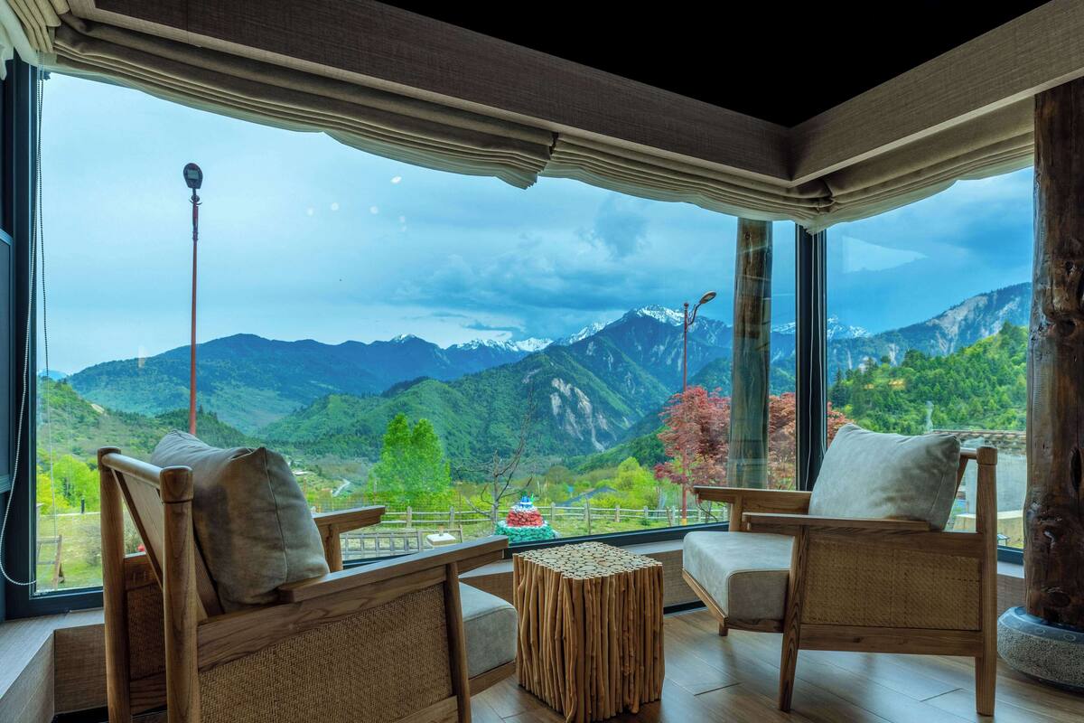 Ein Zimmer mit großem Fenster und Bergblick, Holzmöbel und ein kleiner Tisch.