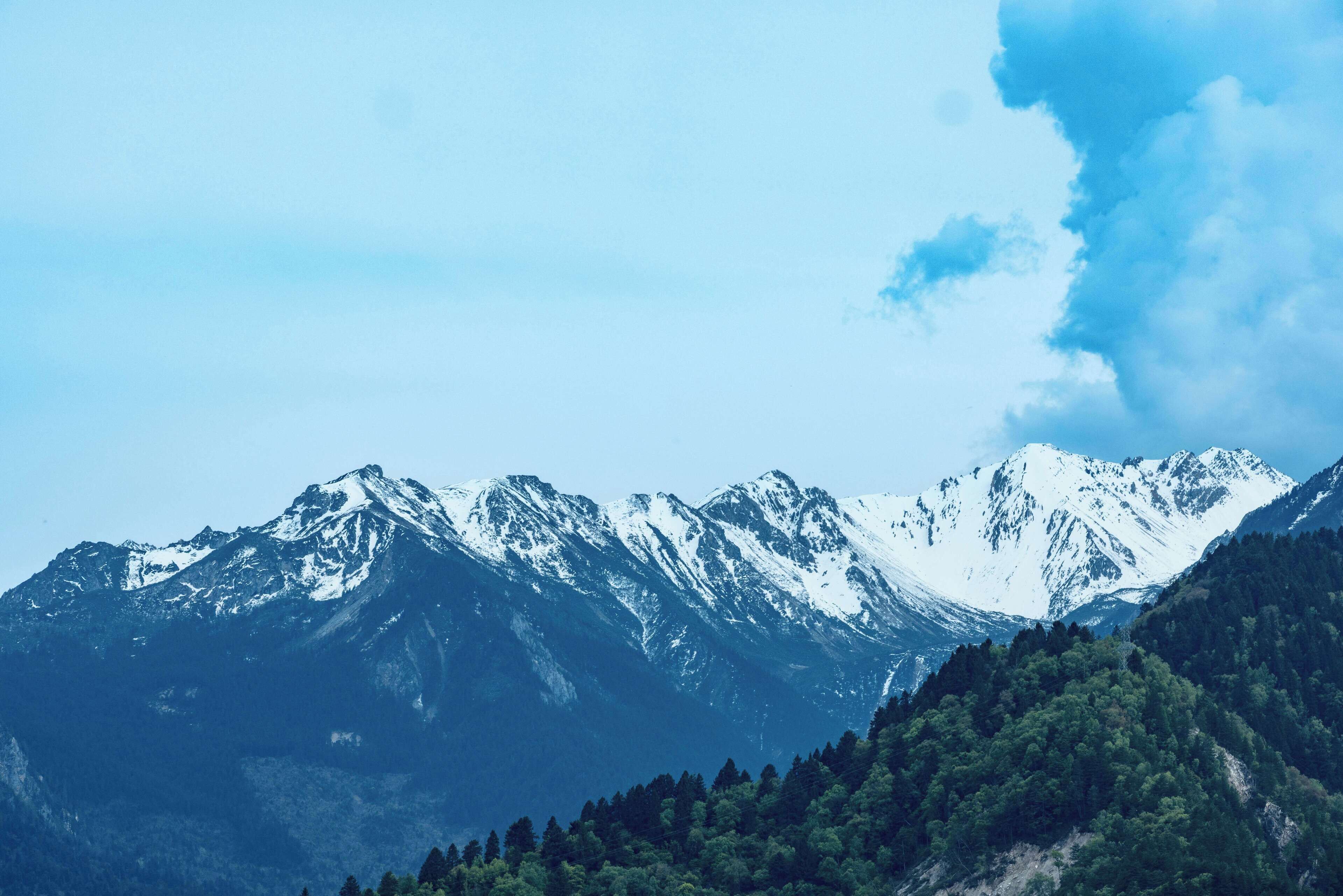 A mountain range with snow-capped peaks and dense forested areas.