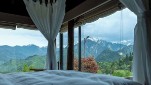 Un dormitorio con una cama grande, vistas a montañas nevadas y un balcón con barandilla de madera.