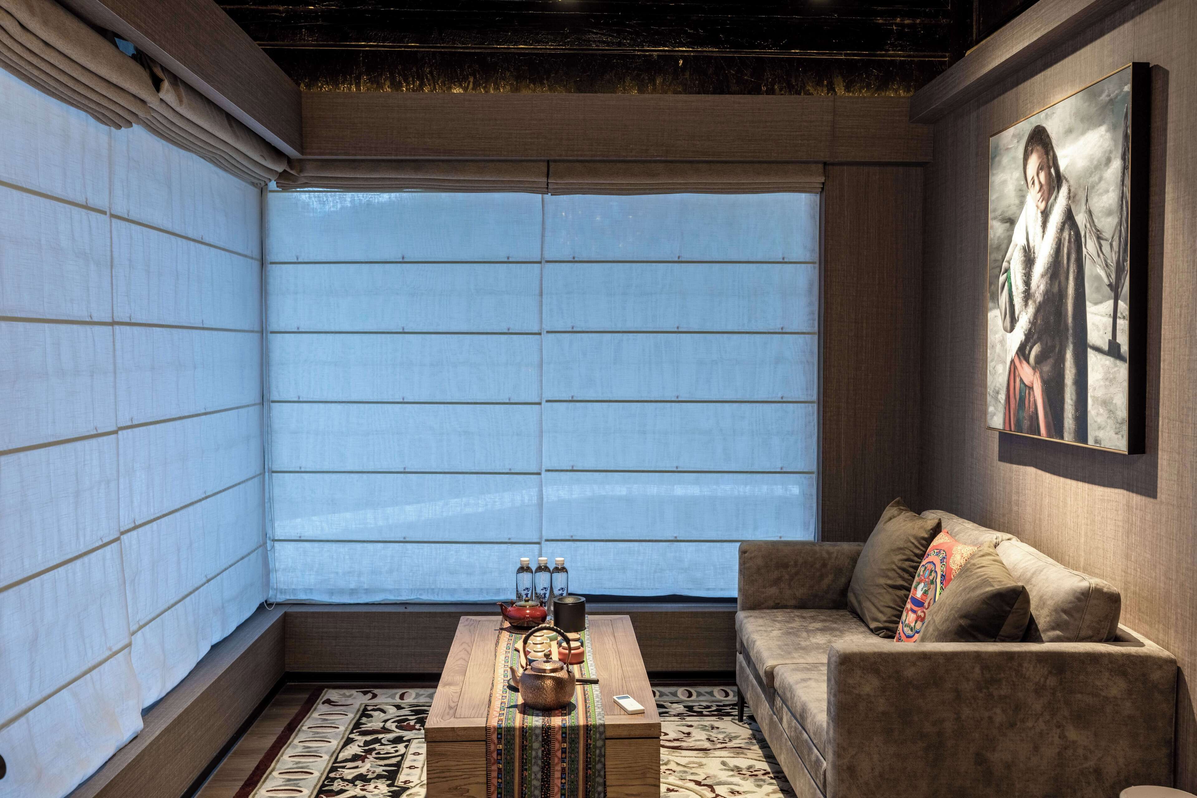 A modern living room with a sofa, a coffee table with decorative items, and a large window with blinds.