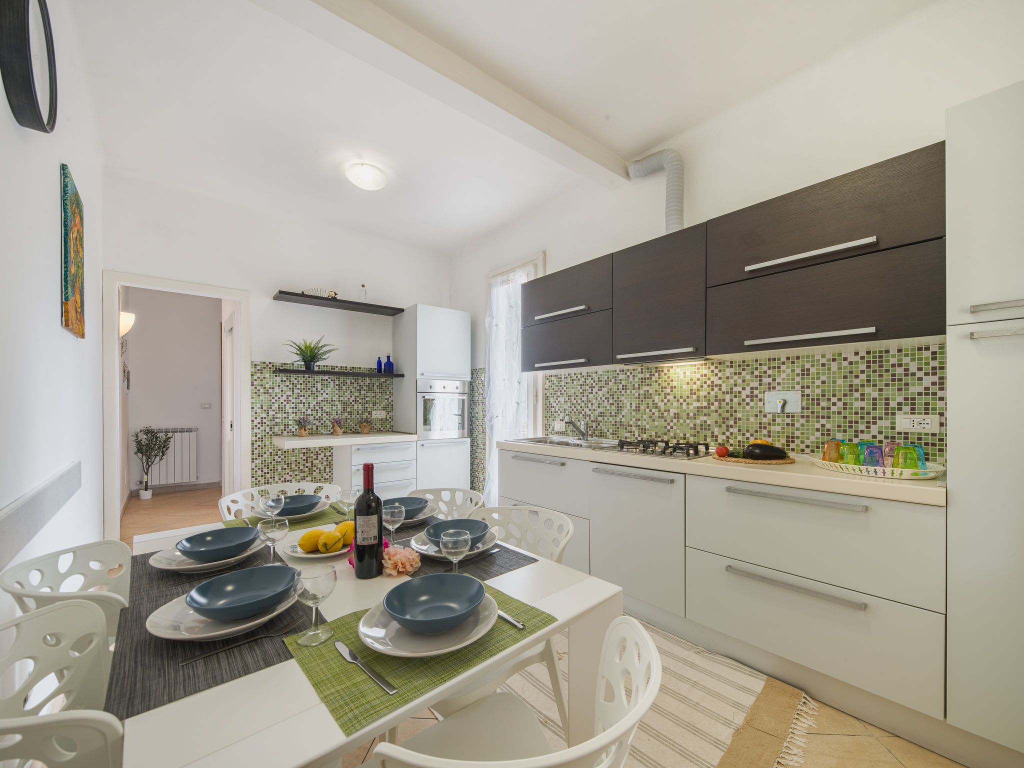 A modern kitchen with white cabinets, a tiled backsplash, and a dining area with a table set for four.