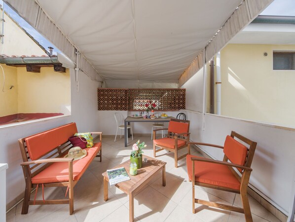 A covered outdoor seating area with wooden furniture and a table, a decorative screen, and a window with a view of the building. - Appartamento La Conchiglia by Interhome (Viareggio)